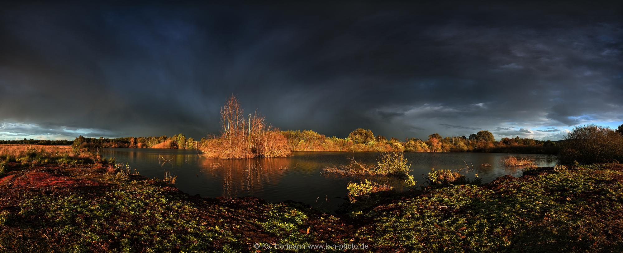 Landschaftspanorama Tiefhängende Regenwolken und das Licht der Abendsonne erzeugen eine dramatische Stimmung über dem Moor.